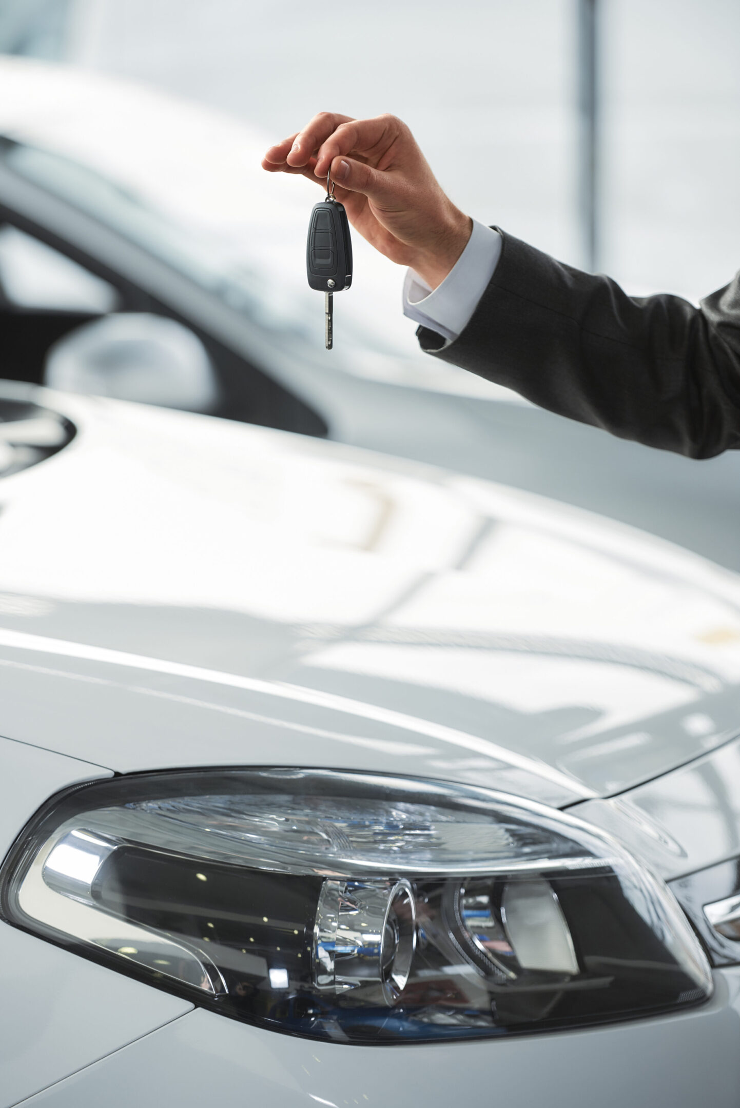 Car salesman is standing at the dealership holding a keys. Close-up.